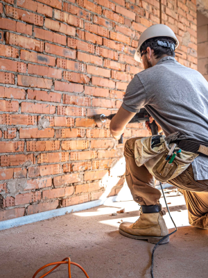 Handyman at a construction site in the process of drilling a wall with a perforator.